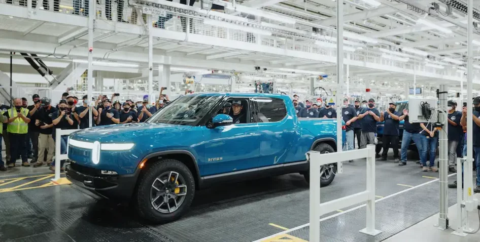 First Rivian electric vehicle driving off factory floor.